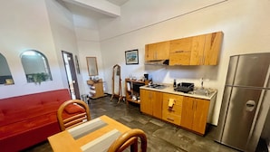 Cozinha compacta com armários de madeira, geladeira de aço inoxidável, mesa de jantar com cadeiras e sofá vermelho.