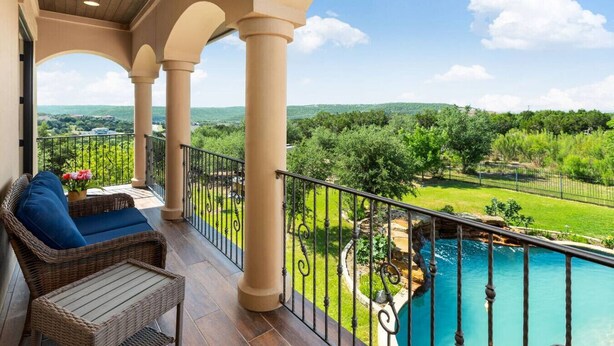 A balcony with wicker furniture, a pool, and a view of a green landscape.