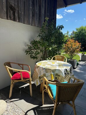 An outdoor patio with wicker chairs and a table covered with a patterned tablecloth.