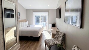 Une chambre d’hôtel moderne avec un grand lit, un coin salon comprenant un fauteuil à motifs, une petite table et un téléviseur fixé au mur.