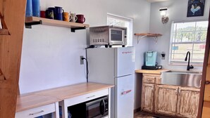 Eine kompakte Küche mit weißen Schränken, einer eingebauten Mikrowelle, einem Kühlschrank und einer Holzarbeitsplatte.