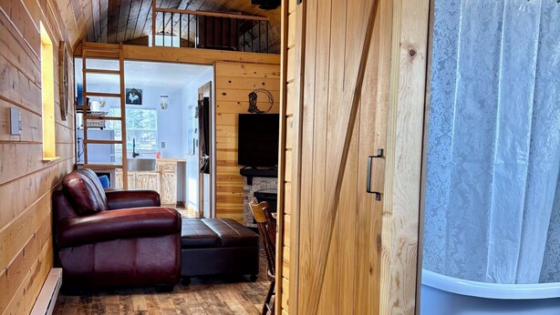 Ein gemütliches Blockhausschlafzimmer mit Holzboden, einer Couch, einem Fernseher und einer Schiebetür zu einem Badezimmer.