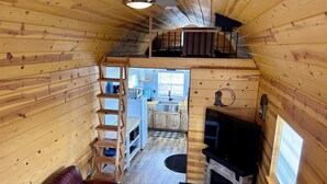 Ein gemütliches Blockhaus-Interieur mit Schlafgalerie, Kamin, Holzleiter und Ledersofa.