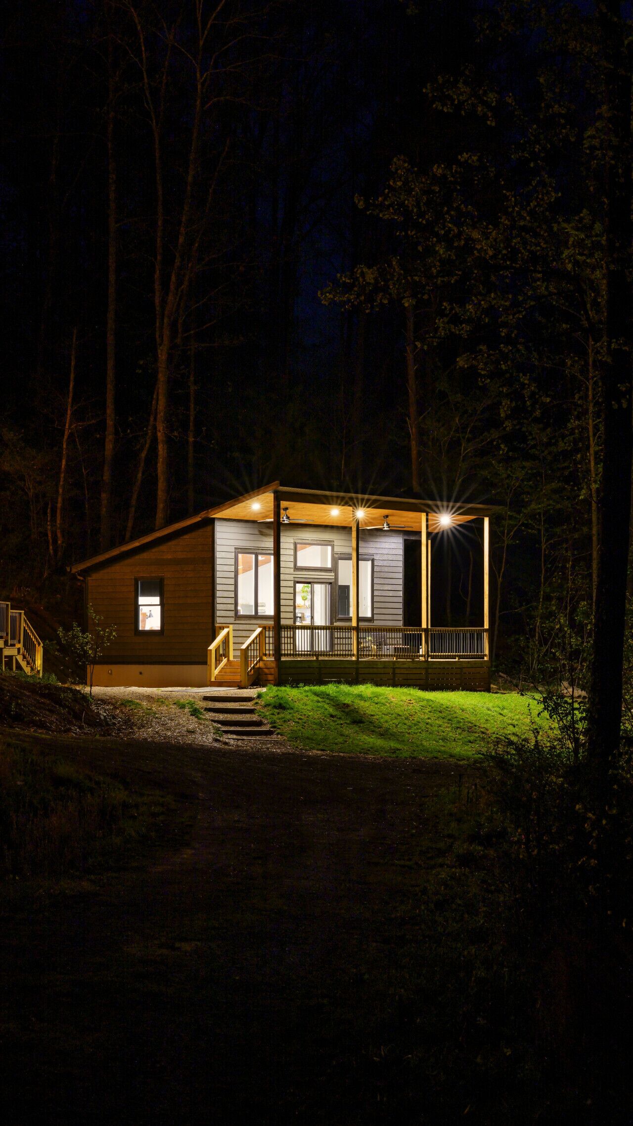 A cabin with a porch, a staircase, and a well-lit entrance.