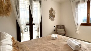 A bedroom with a bed, two windows with sheer curtains, a chair, and a wall-mounted decorative item.