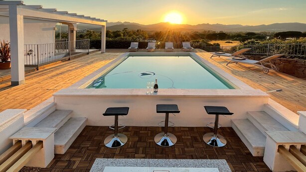 A pool with a sunset view, lounge chairs, and a bar area with stools.