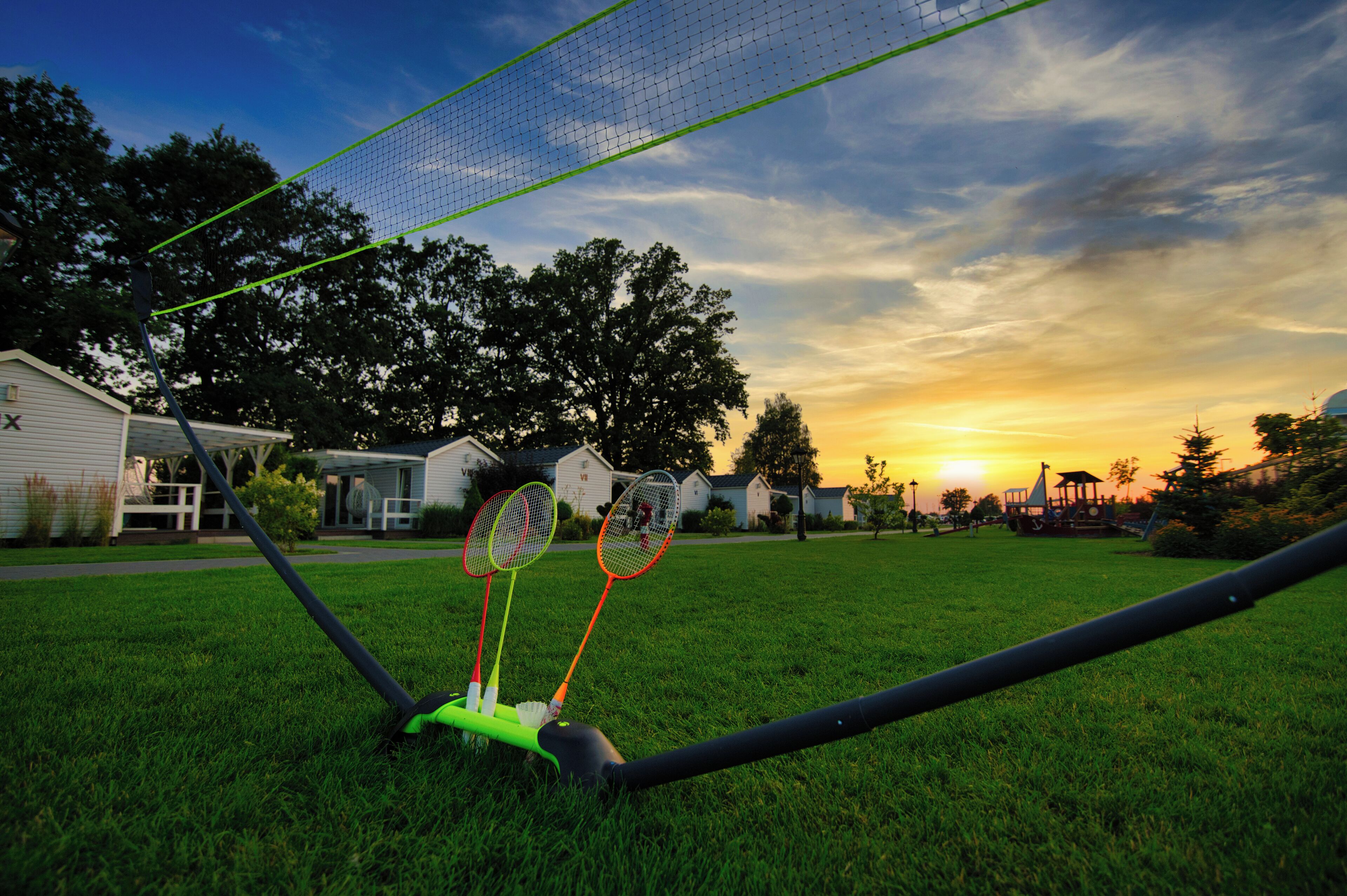 A badminton court with a net, two badminton rackets, and a green shuttlecock holder.