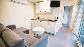 Een kleine woonruimte met een kitchenette, een bank en een rond tafeltje.