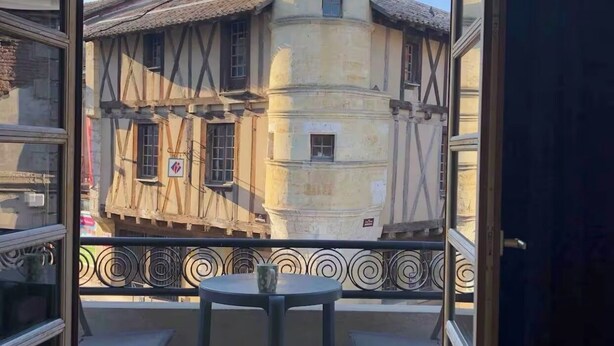 A balcony with a table and chairs, overlooking a historic building with a tower. - House in the heart of a village (Sainte-Foy-la-Grande)