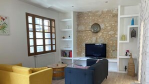A living room with a sofa, a coffee table, a TV, and a stone wall. - House in the heart of a village (Sainte-Foy-la-Grande)