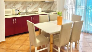 A modern kitchen with beige cabinets, a white countertop, and a dining area with a white table and chairs. - Seaside and spacious Apartment for up to 7 people (Vlorë)