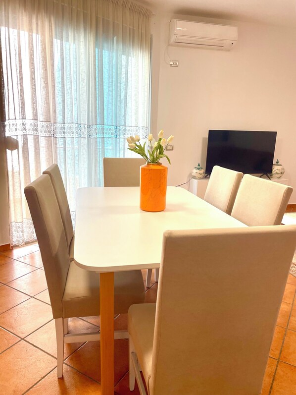 A dining area with a white table, beige chairs, and a vase with white flowers.