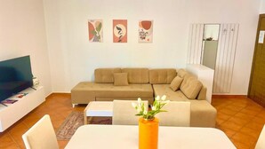 A living room with a beige sectional sofa, a white coffee table, and a TV on a stand. There are three wall art pieces above the sofa. - Seaside and spacious Apartment for up to 7 people (Vlorë)