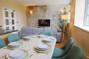 A modern living room with a flat-screen TV, a dining table set for four, and a sofa. - 2 Bed Apartment in Brighton centre | Sleeps 6 (Brighton and Hove)