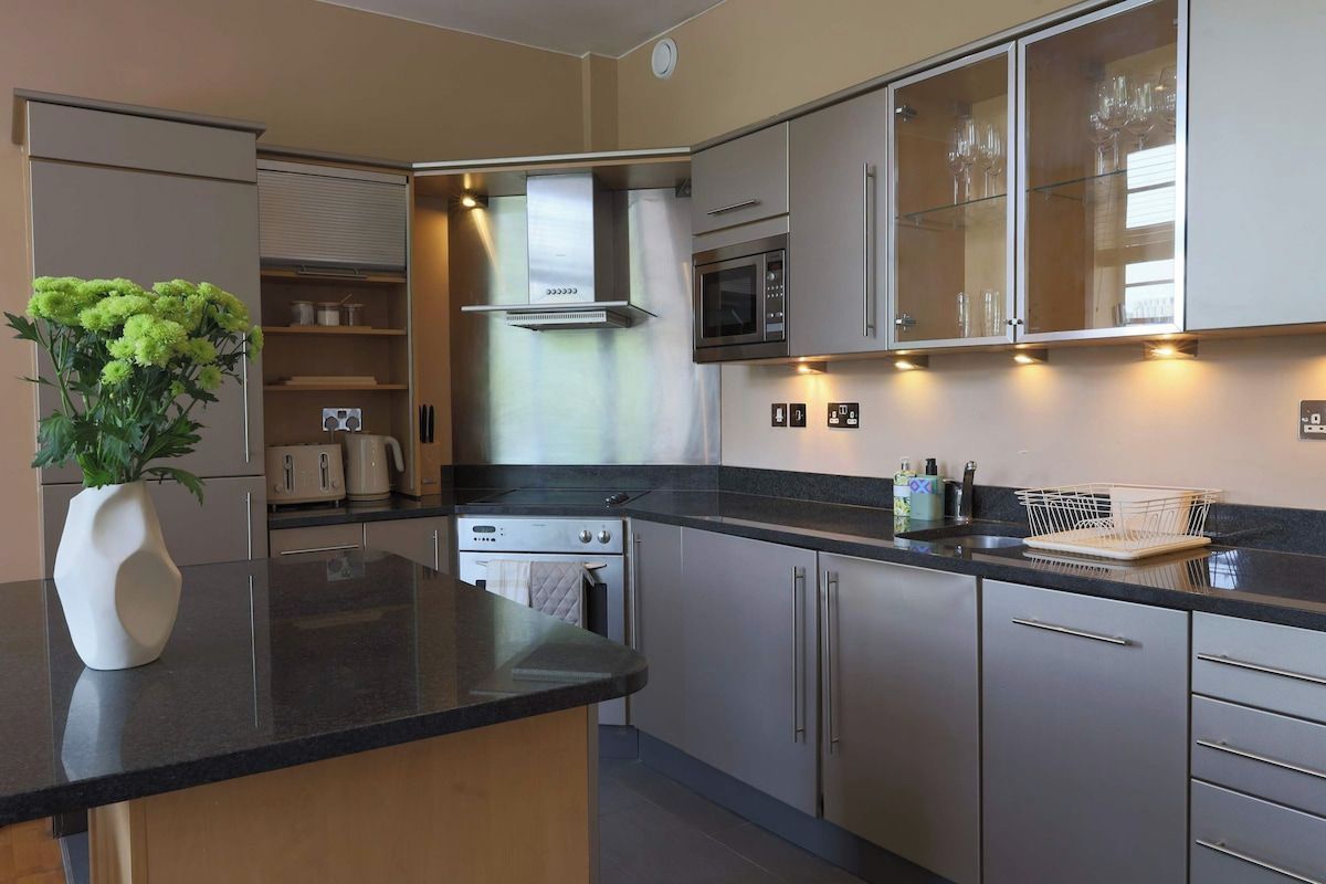 A modern kitchen with stainless steel appliances, a central island, and a glass cabinet with wine glasses.