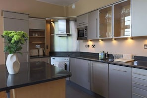 A modern kitchen with stainless steel appliances, a central island, and a glass cabinet with wine glasses. - 2 Bed Apartment in Brighton centre | Sleeps 6 (Brighton and Hove)