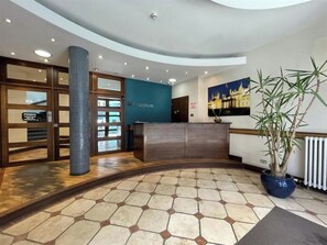 A reception area with a reception desk, a blue wall, a large potted plant, and a tiled floor. - 2 Bed Apartment in Brighton centre | Sleeps 6 (Brighton and Hove)