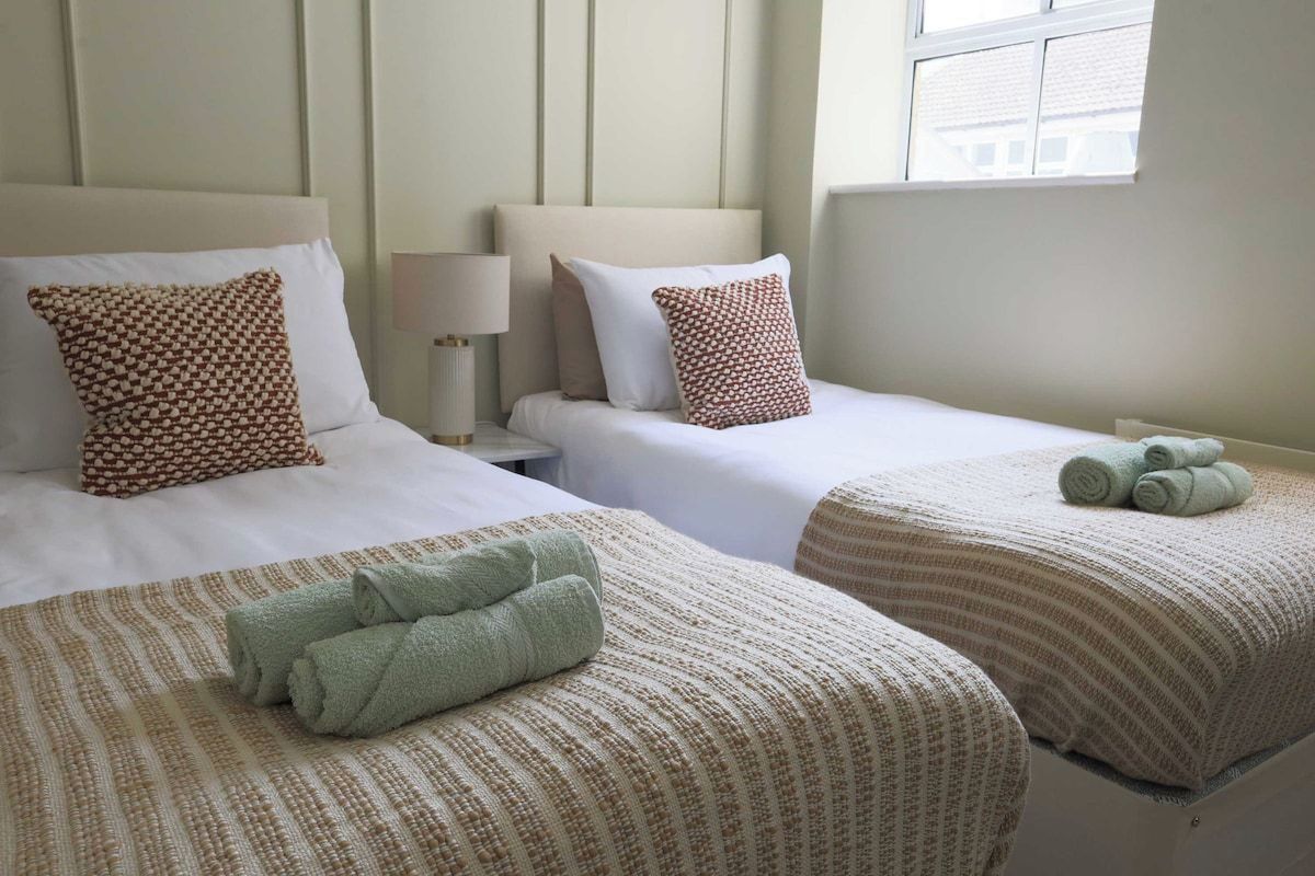 A hotel room with two beds, each with a patterned bedspread and pillows, a bedside lamp, and a window with a view.