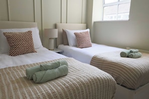 A hotel room with two beds, each with a patterned bedspread and pillows, a bedside lamp, and a window with a view. - 2 Bed Apartment in Brighton centre | Sleeps 6 (Brighton and Hove)