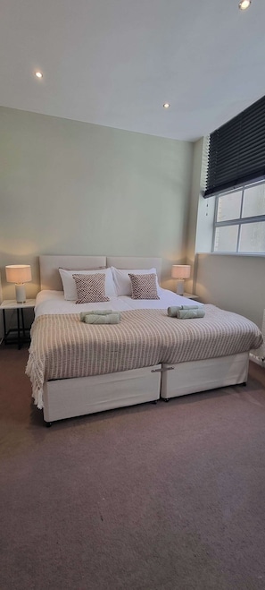 A double bed with a white headboard, two bedside lamps, and a window with blinds. - 2 Bed Apartment in Brighton centre | Sleeps 6 (Brighton and Hove)