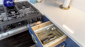 Una cocina con estufa de acero inoxidable, un cajón con organizador de utensilios y un armario azul.
