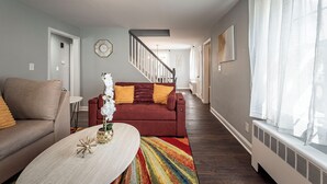 Una sala de estar con un sofá rojo, un sofá beige, una mesa de centro y una escalera que lleva a otra habitación.