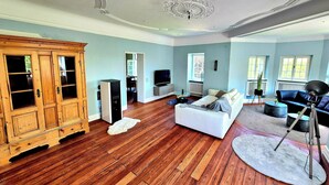 Un salon spacieux doté d’un parquet, d’un canapé blanc, d’un canapé bleu, d’un meuble en bois et d’un ventilateur de plafond.