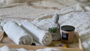 Een netjes opgemaakt bed met opgerolde handdoeken, een klein Boeddhabeeldje en een verpakking warme vanille-verzorgingslotion.