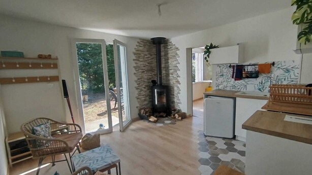 Een ruime woonkamer met een open haard, een eettafel en een keuken voorzien van een koelkast en een spoelbak.