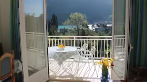 A balcony with a table and chairs, a vase with flowers, and a view of mountains and a lake. - Apartments Doko Zaton Bay (Zaton)