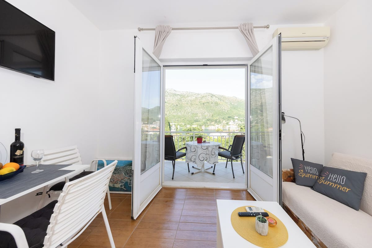 Een balkon met een tafel, stoelen, een bank, een televisie en een airconditioning.