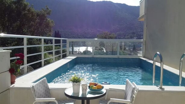 An outdoor swimming pool with a glass barrier, a table with a bowl of fruit, and a chair. - Apartments Doko Zaton Bay (Zaton)