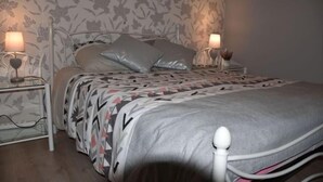 A bedroom with a bed, two bedside tables, and floral wallpaper. - Gite des Bords de rance (Pleudihen-sur-Rance)