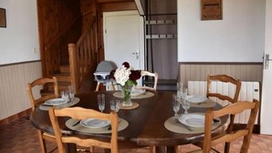 A dining area with a wooden table set for six, surrounded by wooden chairs. A vase with flowers is on the table, and a staircase is visible in the background. - Gite des Bords de rance (Pleudihen-sur-Rance)