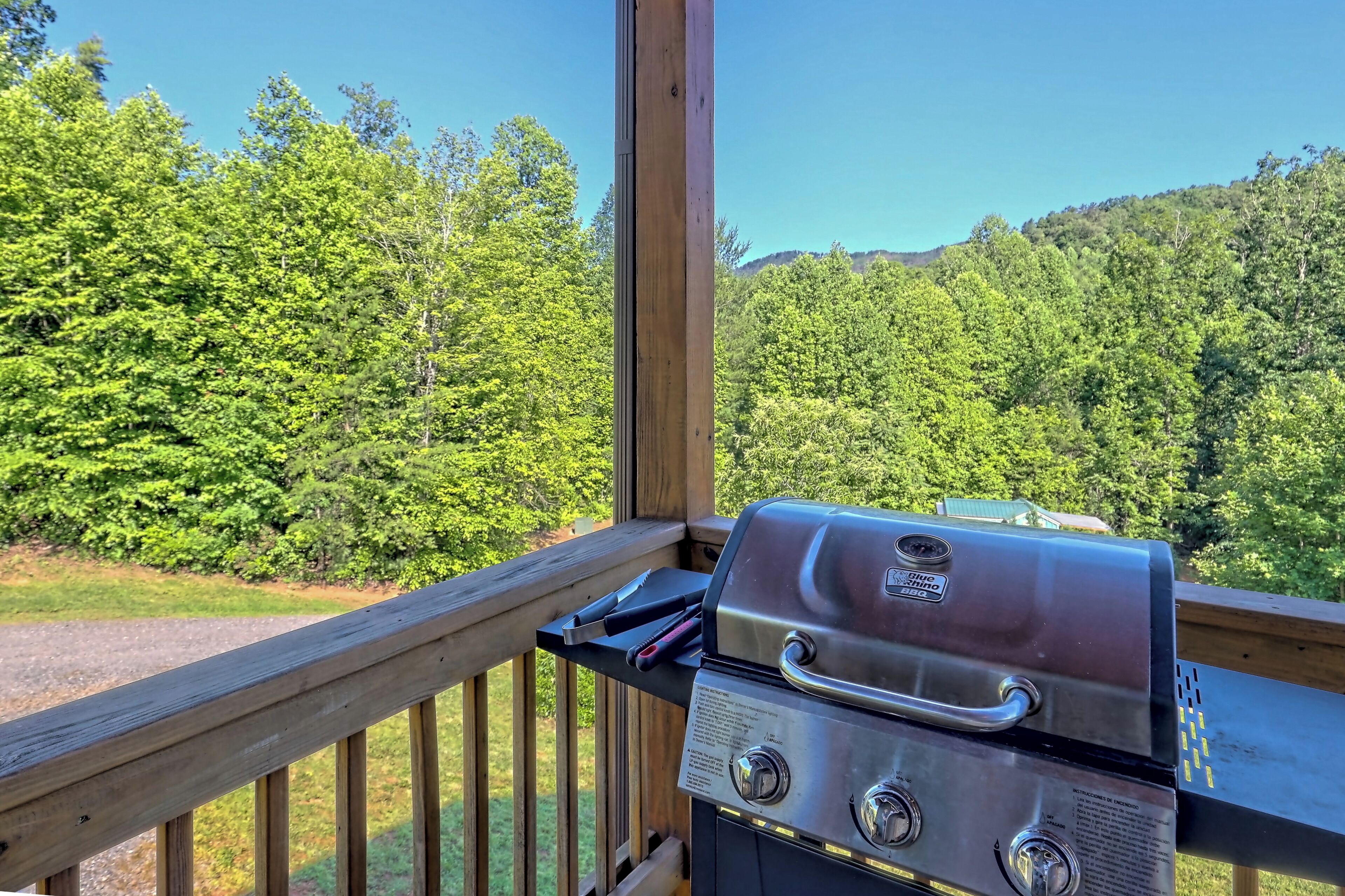 Ein Grill auf einer Holzterrasse mit Blick auf eine bewaldete Landschaft.