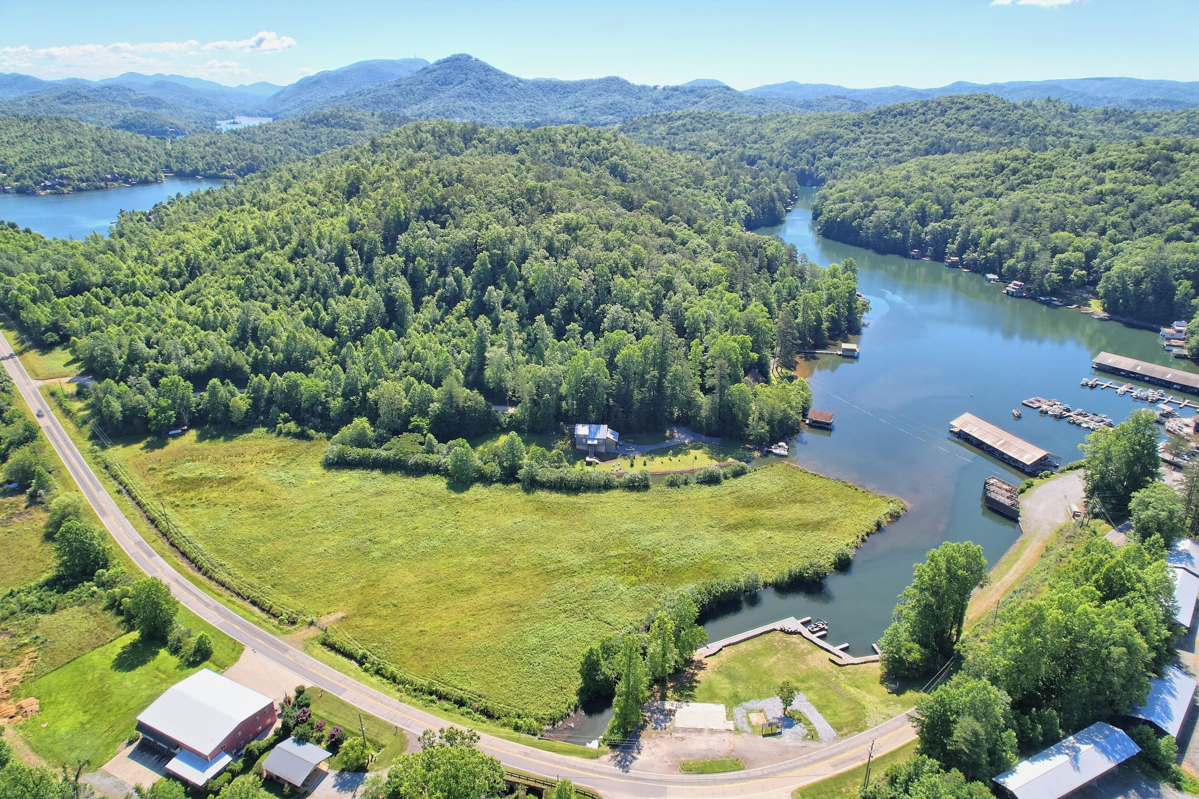 An aerial view of a lakeside property with a dock, a road, and a large green field.