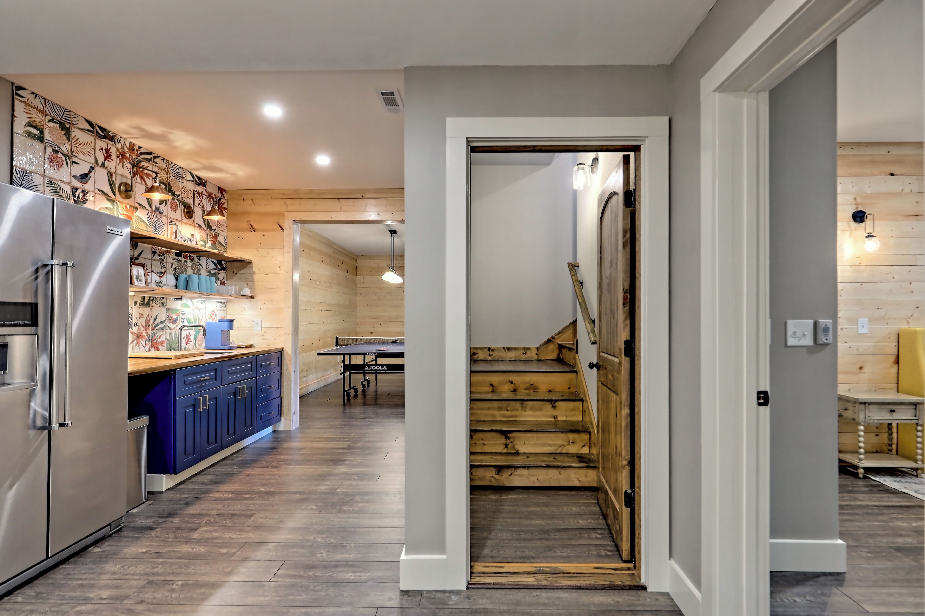 A modern kitchen with a refrigerator, blue cabinets, and a wooden staircase leading to another room.