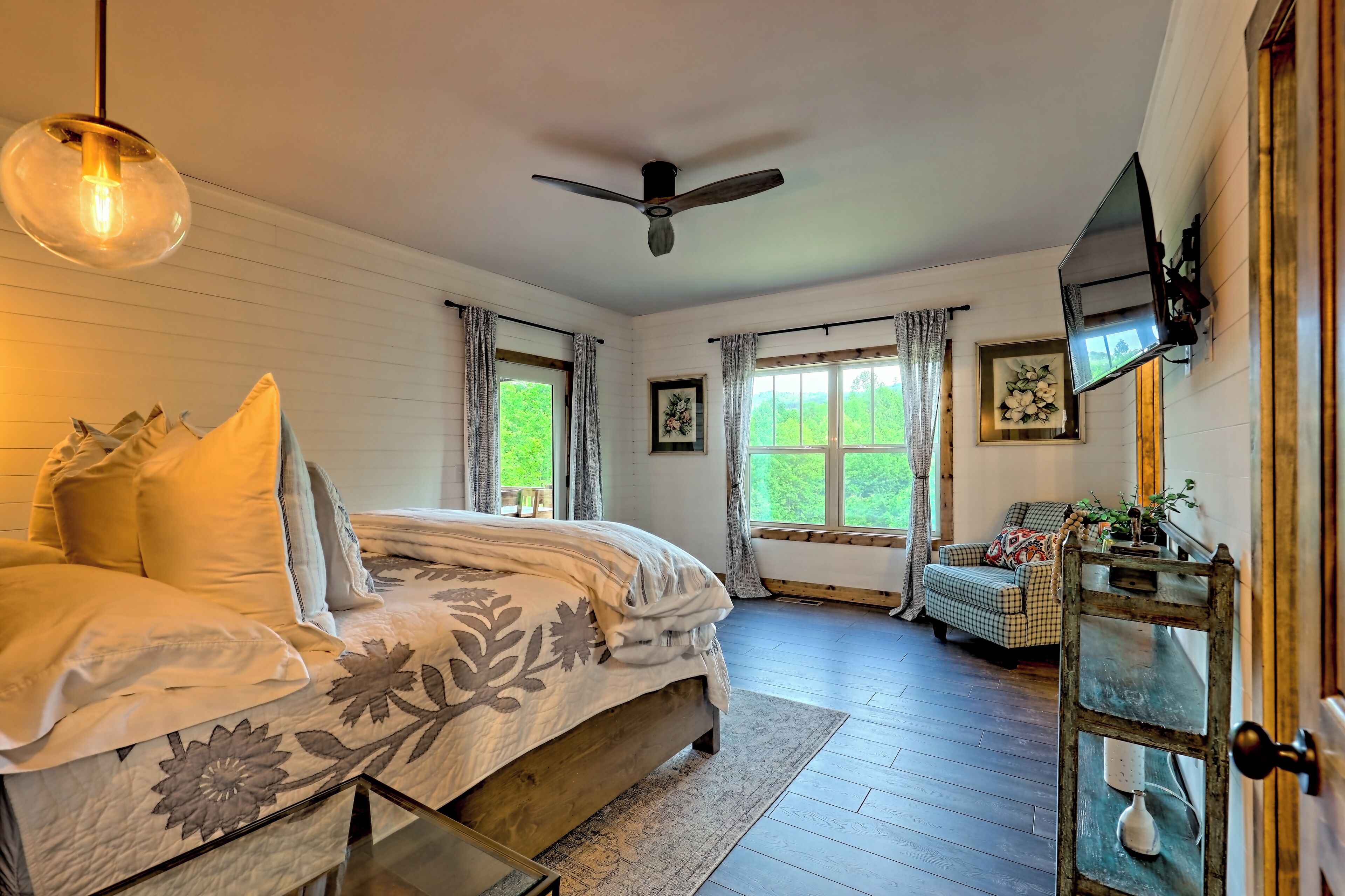 A bedroom with a bed, a ceiling fan, a TV, and a window with curtains.