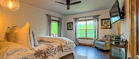 A bedroom with a bed, a ceiling fan, a TV, and a window with curtains.