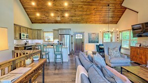 Un vaste espace de vie doté d’un plafond en bois, une cuisine équipée d’appareils électroménagers modernes et un coin salon confortable avec un canapé et des fauteuils.