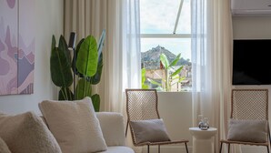 A modern living room with a sofa, two wicker chairs, a small side table, and a large window with a view of a hill. - Acropolis Dream with Plunge Pool (Athina)