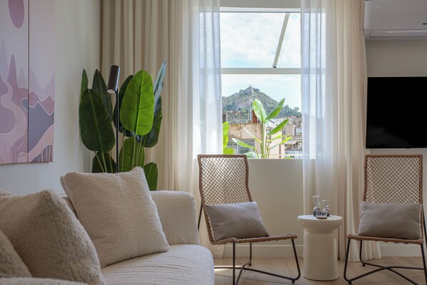 A modern living room with a sofa, two wicker chairs, a small side table, and a large window with a view of a hill.