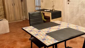 A dining area with a table, chairs, a television mounted on the wall, a clock, and a wardrobe.