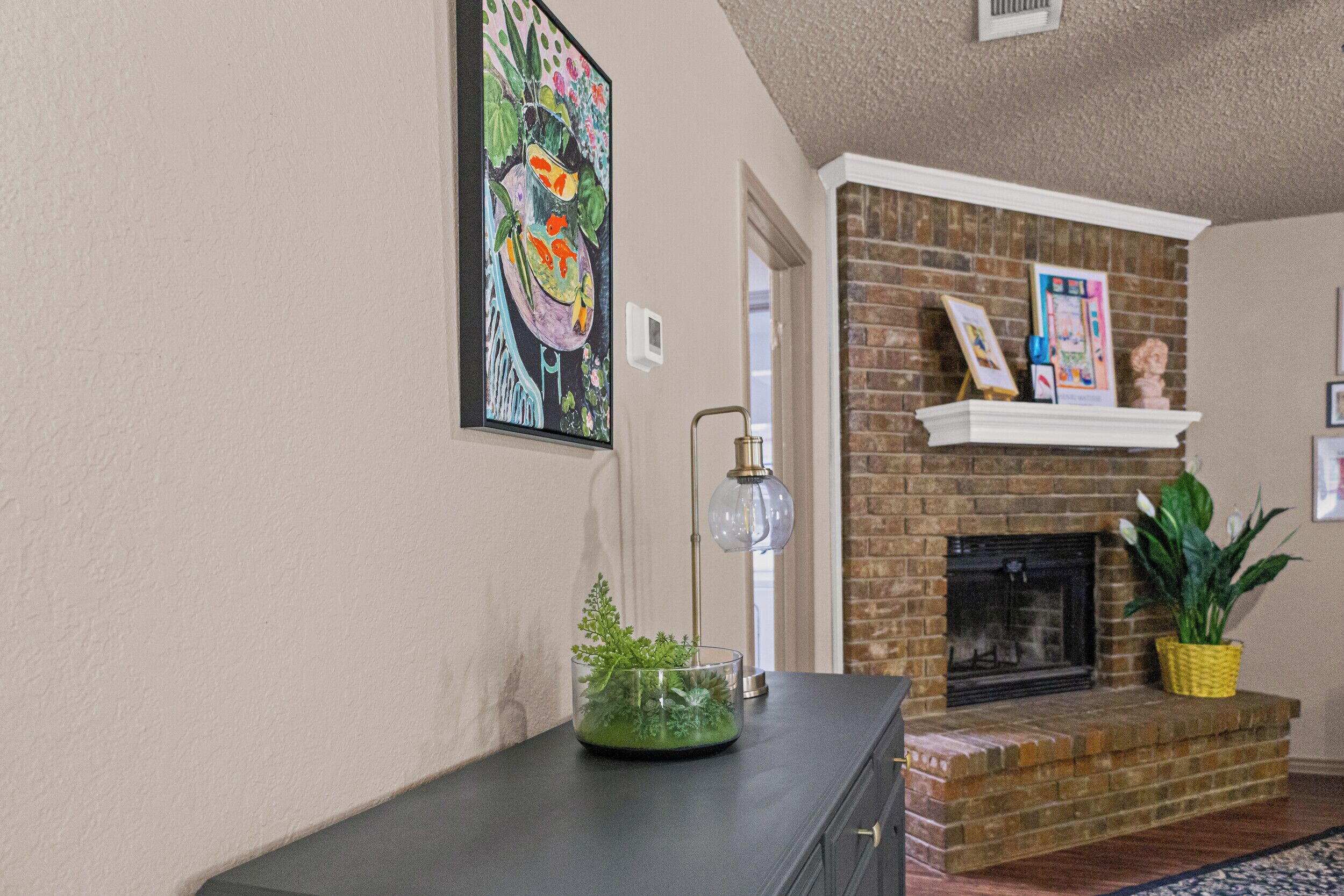 A living room with a fireplace, a dark wooden cabinet, and a clear glass vase with green plants.