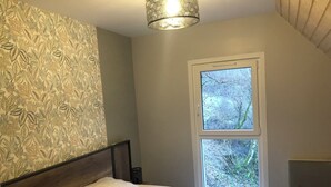 Un dormitorio con cama, una ventana con vistas a árboles, un papel tapiz estampado y una lámpara colgante.