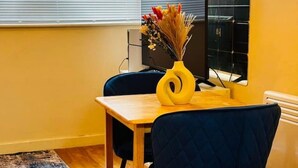 Una piccola zona pranzo con un tavolo di legno, una sedia blu e un vaso giallo con fiori secchi.