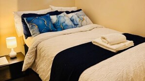 Un letto rifatto con cura, un cuscino a motivi blu e bianchi, una coperta bianca e un asciugamano piegato di colore bianco sul lato.