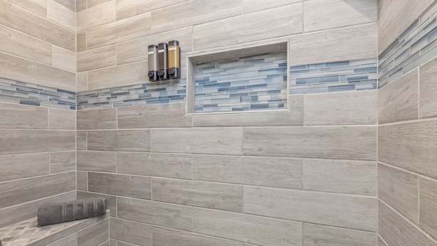 A shower area with grey tiles and a small shelf with toiletries.