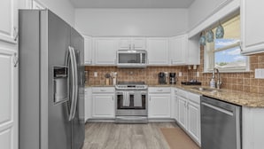 A modern kitchen with stainless steel appliances, white cabinetry, and a brown tiled backsplash.