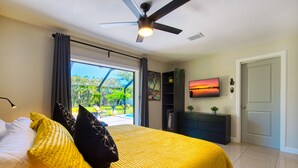 Une chambre à coucher avec un lit, un ventilateur de plafond, une télévision, une armoire et une vue sur l’extérieur.
